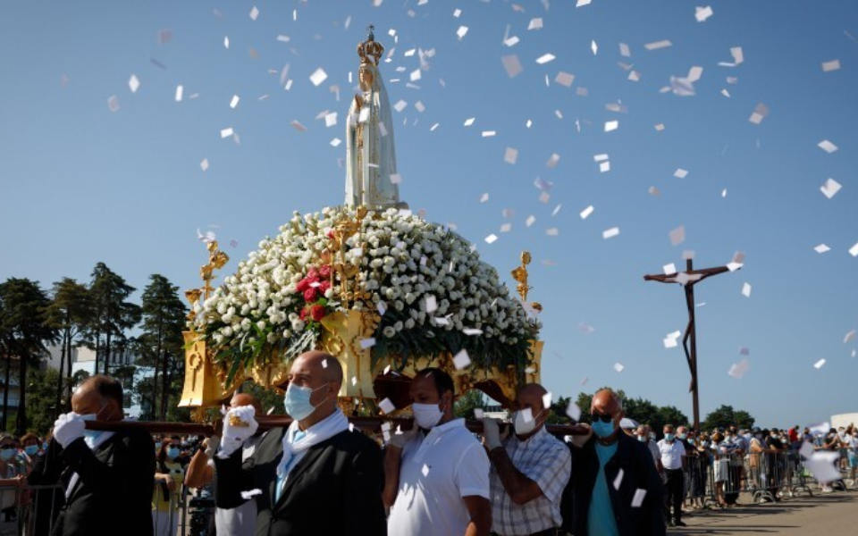 Our Lady of Fátima statue carried in a procession, surrounded by flowers and falling petals