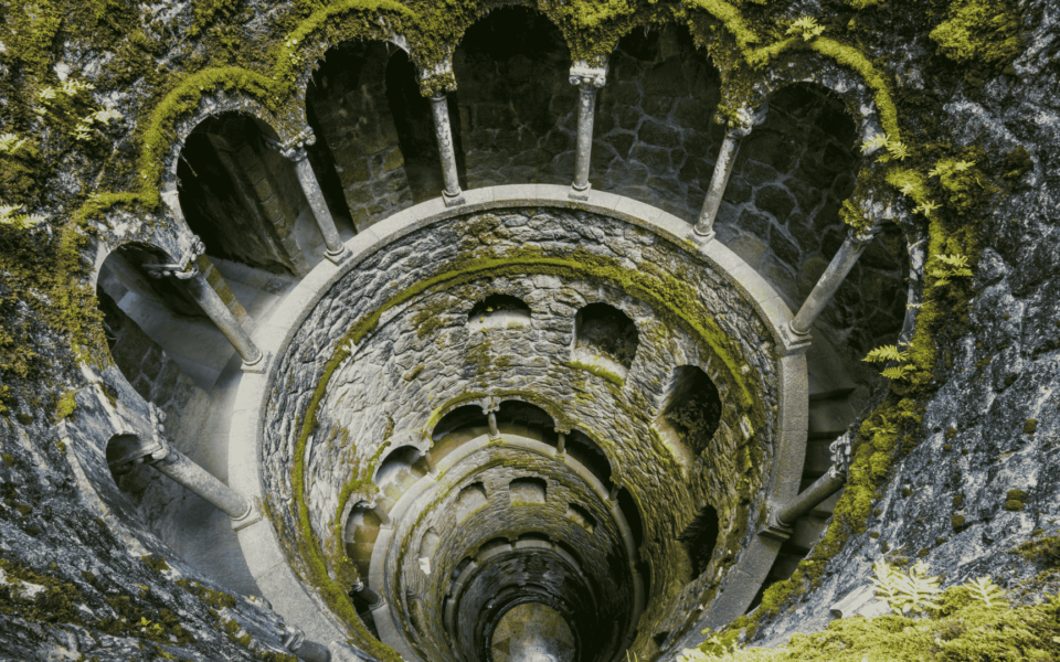 Spiral view of the Initiation Well at Quinta da Regaleira in Sintra, Portugal, showcasing its mystical architecture and moss-covered stone walls.