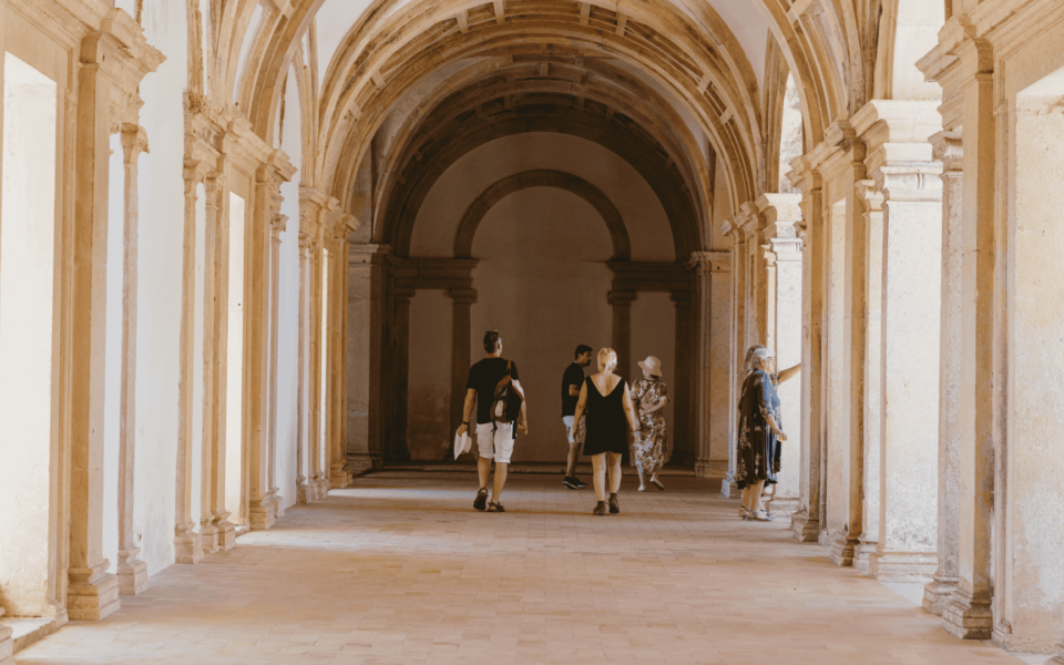 Tourists walking through the arched stone corridor inside the Convent of Christ in Tomar, Portugal, under vaulted ceilings and soft natural light.