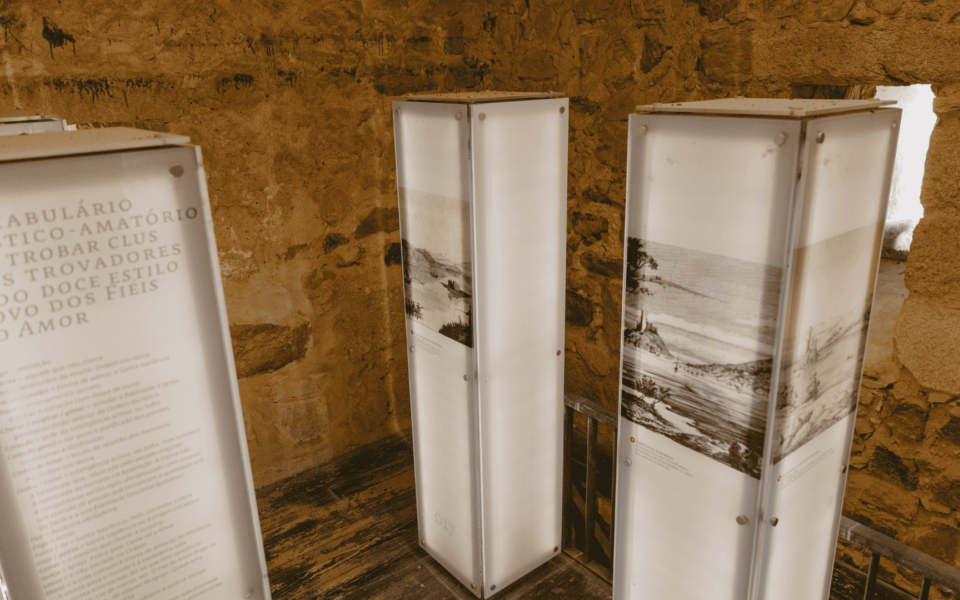 Exhibition display inside Almourol Castle, Portugal, showcasing poetic vocabulary from the troubadour tradition and historical illustrations on illuminated panels.