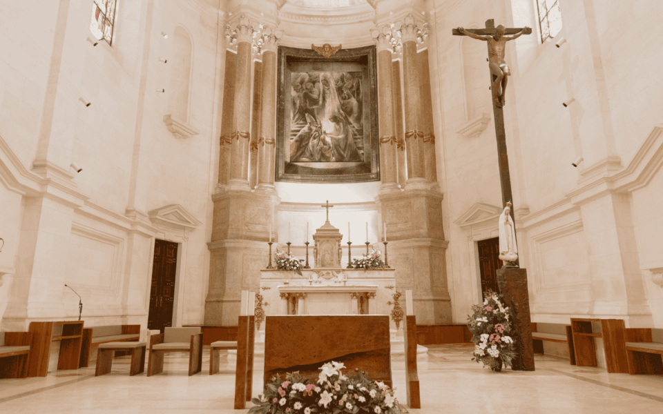 Ornate interior of the Basilica of Our Lady of the Rosary in Fátima, Portugal, featuring a marble altar, floral arrangements, crucifix and classical religious artwork.
