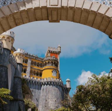 Colorful view of Pena Palace framed by a traditional Portuguese tiled arch in Sintra, Portugal, under a clear blue sky.