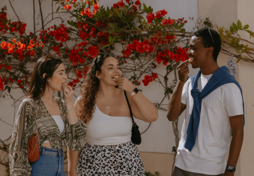 Group of friends enjoying traditional Portuguese sweets in a picturesque street with red bougainvillea flowers in the background.