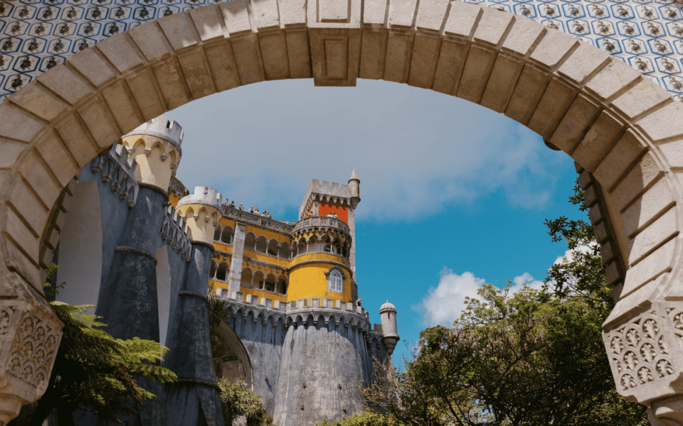 Colorful view of Pena Palace framed by a traditional Portuguese tiled arch in Sintra, Portugal, under a clear blue sky.