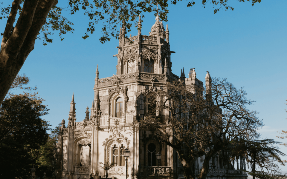 Gothic-inspired main palace of Quinta da Regaleira in Sintra, Portugal, surrounded by lush trees under a clear blue sky.