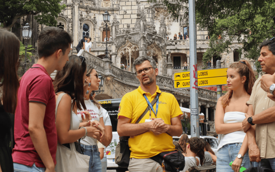 Tour guide giving historical context to a group of tourists at the entrance of Quinta da Regaleira in Sintra, Portugal, with the palace's ornate façade in the background.
