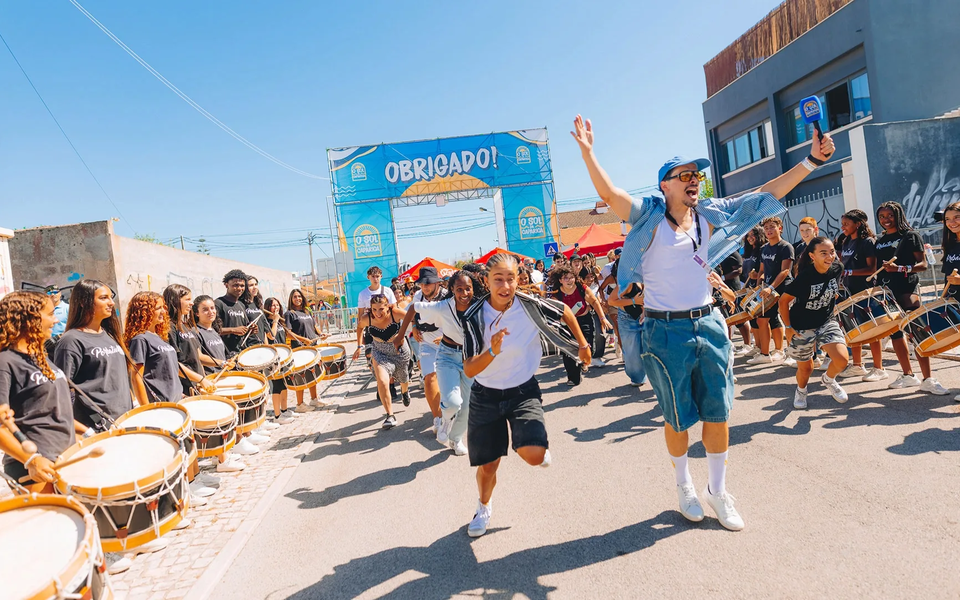 Colorful entrance at O Sol da Caparica Festival in Portugal, with drummers, dancers, and people celebrating under a bright summer sky