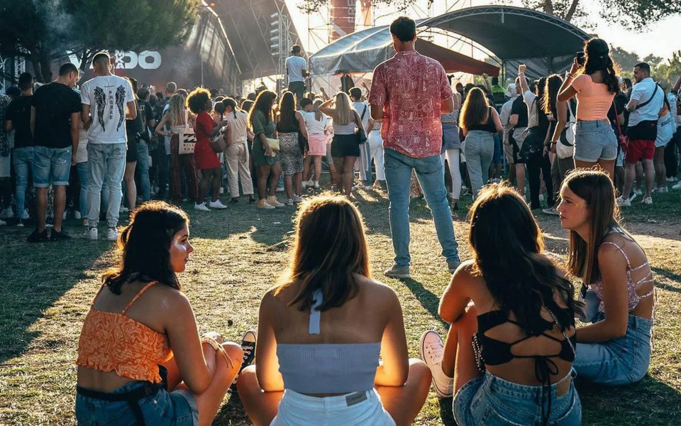 Young people enjoying the atmosphere at O Sol da Caparica Festival in Portugal, sitting on the grass with the stage in the background.