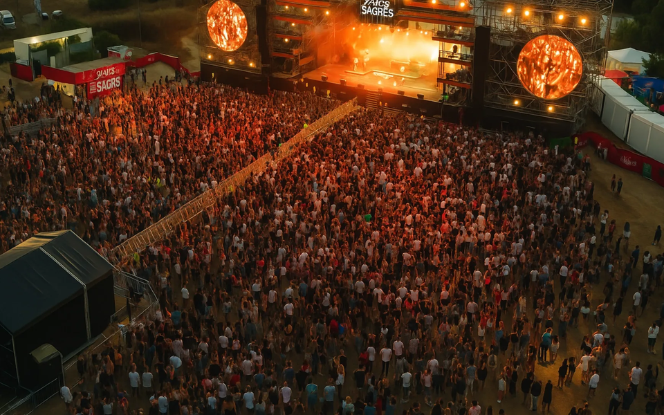 Aerial view of a music festival in Portugal at sunset, with a large crowd gathered in front of a brightly lit stage