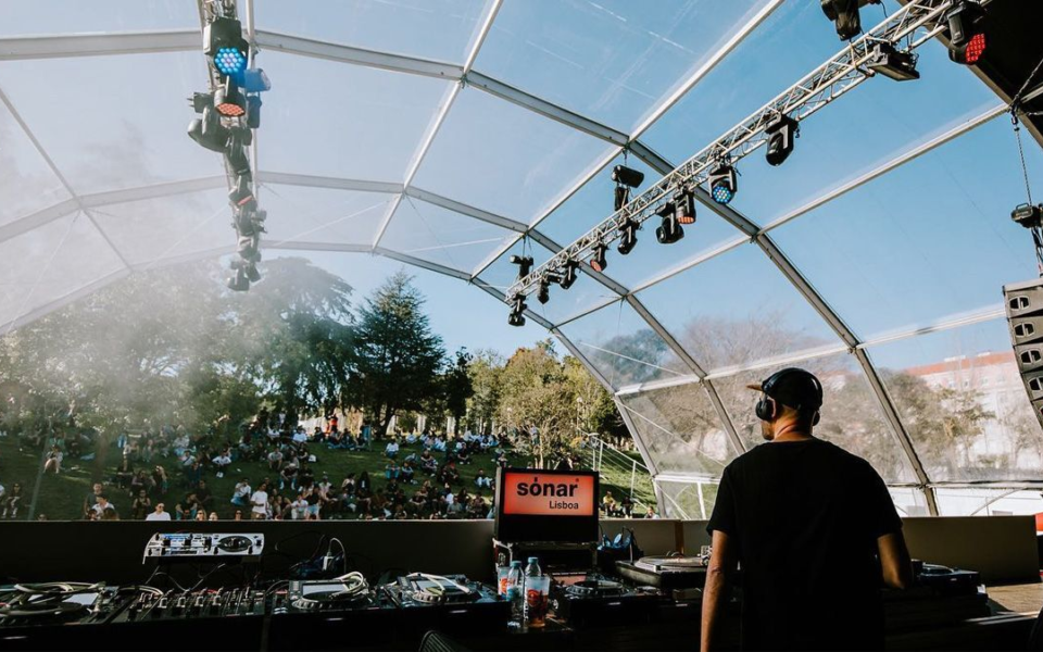 DJ performing on stage at Sónar Lisboa with people seated on the grass