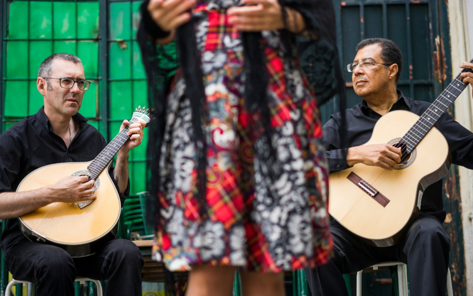 Musicians playing Portuguese and classical guitar while a fado singer performs in a traditional Lisbon setting