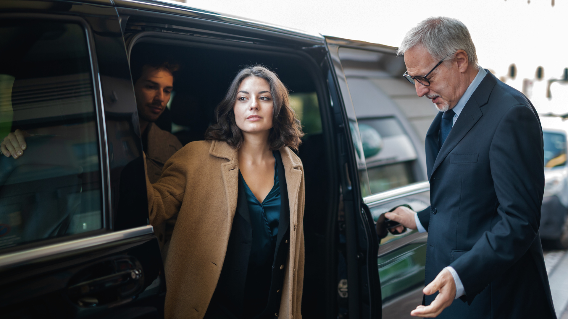 Elegant woman exiting a luxury vehicle with assistance from a private chauffeur in suit, representing a premium transfer or VIP transport service.