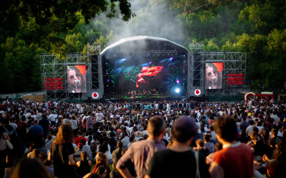 Large crowd enjoying a concert at Vodafone Paredes de Coura Festival in Portugal, with a big stage and forest backdrop.