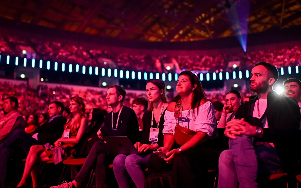 Focused audience members watching a talk at the Web Summit in Lisbon’s Altice Arena, surrounded by dramatic red and blue lighting.